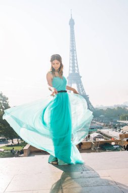 Paris 'teki Eyfel Kulesi' nin arka planında mavi ve yeşil elbiseli güzel ve zarif bir kız duruyor.
