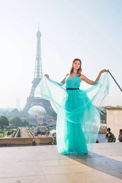 パリのエッフェル塔を背景に 青と緑のドレスの若い美しくエレガントな女の子が立っています フランス — ストック写真