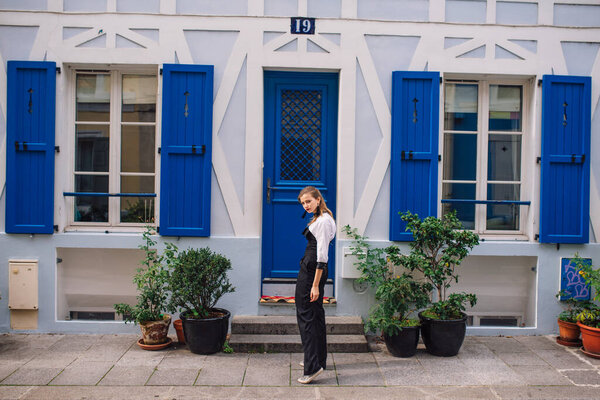 Красивая молодая женщина в черном модном комбинезоне стоит на парижской улице с яркими цветами.
