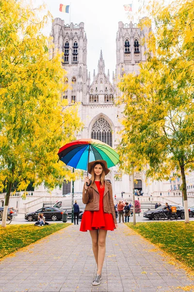 Girl with an umbrella standing at the man square or Grand Platz in Brussel, Belgium with a cathedral behind her.