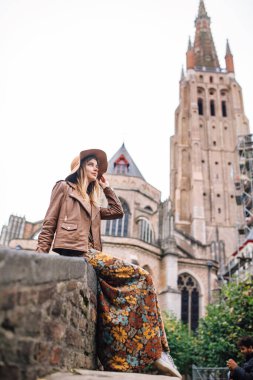 Bir kız Boniface Köprüsü 'nde oturuyor. Belçika' nın Bruges kentindeki Vrouwekerk Kilisesi 'ne bakıyor..