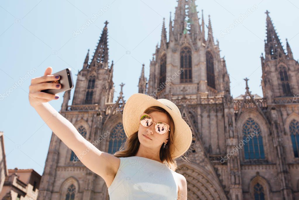 A young and happy tourist takes a selfie photo in front of the Cathedral of the Holy Trinity Barcelona