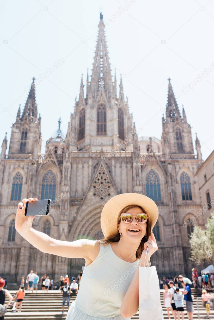 A young and happy tourist takes a selfie photo in front of the Cathedral of the Holy Trinity Barcelona