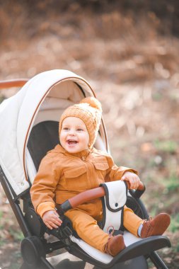 Sevimli, güzel bir çocuk bir bebek arabasında oturuyor ve gülümsüyor ve annesini bekliyor.