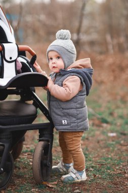 Bir yaşındaki bir çocuk pistte ilk adımlarını atıyor. Gri bir yelek ve bej pantolon giymiş seçici bir odak noktası var.