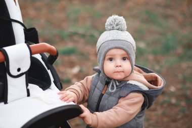 Bir yaşındaki bir çocuk pistte ilk adımlarını atıyor. Gri bir yelek ve bej pantolon giymiş seçici bir odak noktası var.