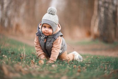 Küçük bir çocuk, gri bir jöle ile orman yolunda oturuyor ve kameraya merakla bakıyor.