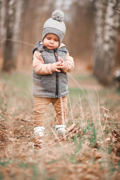 Bir yaşındaki bir çocuk pistte ilk adımlarını atıyor. Gri bir yelek ve bej pantolon giymiş seçici bir odak noktası var.