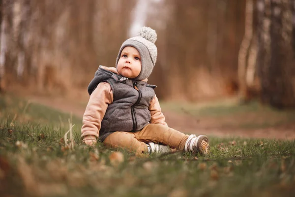 a small boy is sitting on a forest path in a gray jelly and looks curiously at the camera