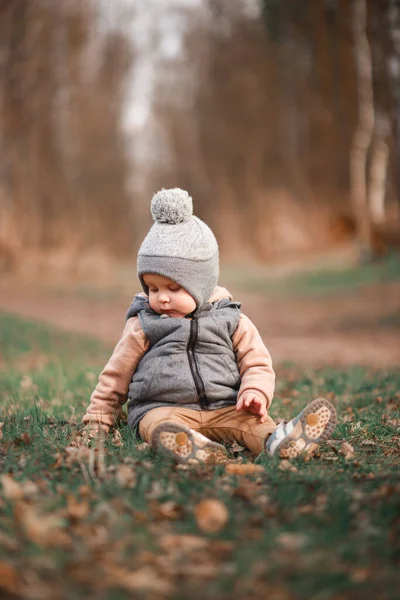 a small boy is sitting on a forest path in a gray jelly and looks curiously at the ground