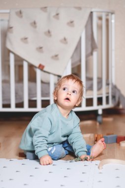 Bir çocuk odasında nane rengi kapüşonlu kazağıyla oynuyor.