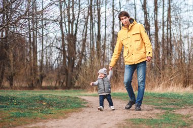 Bir adam parkta yürürken çocuğunu anaokuluna götürür.