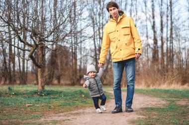 Bir adam parkta yürürken çocuğunu anaokuluna götürür.