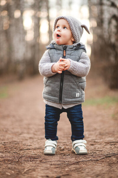 a boy in a gray warm vest and a gray cap plays games in the open air against the background of the spring landscape.