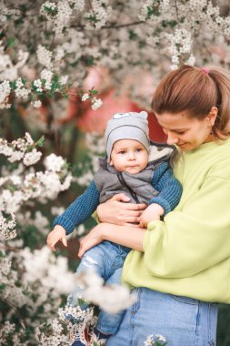 Bir anne, çiçek açan bir ağacın arka planında bir çocukla oynar ve konuşur. Mutlu gülümseyen insanlar.