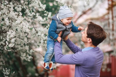 Mutlu baba ve oğul baharda bahçede çiçek açan ağaçların arkasında durur.