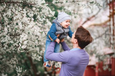 Mutlu baba ve oğul baharda bahçede çiçek açan ağaçların arkasında durur.