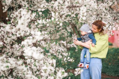 Mutlu anne ve oğul çiçek açan bir ağacın arka planında oynuyorlar. Bahar, Anneler Günü. Mutlu aile