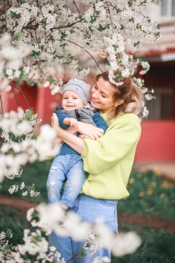 Mutlu anne ve oğul çiçek açan bir ağacın arka planında oynuyorlar. Bahar, Anneler Günü. Mutlu aile