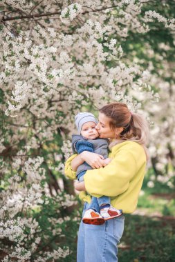 Mutlu anne ve oğul çiçek açan bir ağacın arka planında oynuyorlar. Bahar, Anneler Günü. Mutlu aile