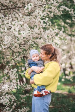 Mutlu anne ve oğul çiçek açan bir ağacın arka planında oynuyorlar. Bahar, Anneler Günü. Mutlu aile