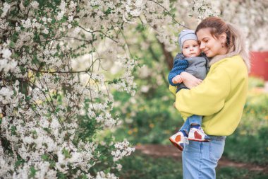 Mutlu anne ve oğul çiçek açan bir ağacın arka planında oynuyorlar. Bahar, Anneler Günü. Mutlu aile