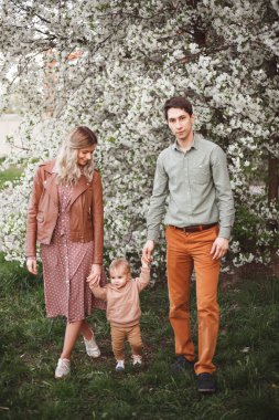 Mutlu ebeveynler, anne ve baba ve oğul baharda bahçede elma ve kiraz ağaçlarının arka planında dururlar.