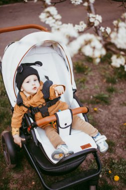 Bej ceketli bir bebek, bebek arabasıyla bahar parkında yürüyor..