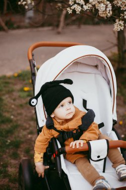 Bej ceketli bir bebek, bebek arabasıyla bahar parkında yürüyor..