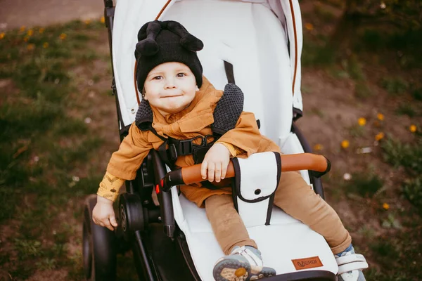 Bej ceketli bir bebek, bebek arabasıyla bahar parkında yürüyor..