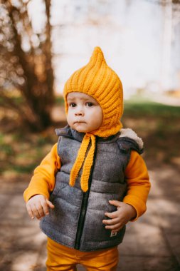 Sarı şapkalı, sarı pantolonlu ve doğanın arka planında gri jöleli şık bir çocuk.