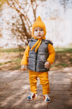 Sarı şapkalı, sarı pantolonlu ve doğanın arka planında gri jöleli şık bir çocuk.