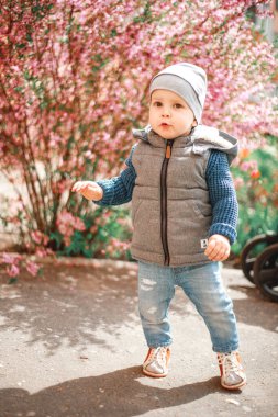 Kot giymiş bir çocuk İlkbaharda çiçekli bir çalılığın yanında duruyor