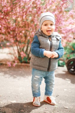 Kot giymiş bir çocuk İlkbaharda çiçekli bir çalılığın yanında duruyor