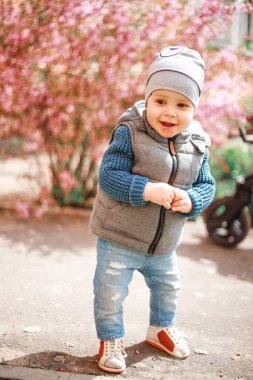 Kot giymiş bir çocuk İlkbaharda çiçekli bir çalılığın yanında duruyor