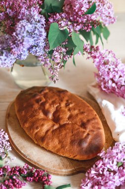 Ev yapımı elmalı turta bir kase leylağın yanındaki ahşap masada. Yumuşak tonlama. Seçici odak.