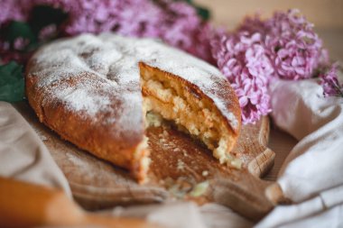 Ev yapımı elmalı turta bir kase leylağın yanındaki ahşap masada. Yumuşak tonlama. Seçici odak.