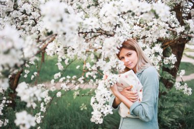 Bir kız izin gününde yüzünde sıradan bir ifadeyle büyük bir yastığa sarılıyor baharda çiçek açan bir elma bahçesinde mavi pijama giyiyor..