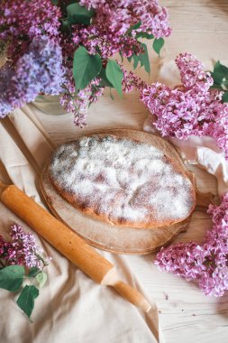 Ev yapımı elmalı turta bir kase leylağın yanındaki ahşap masada. Yumuşak tonlama. Seçici odak.