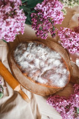 Ev yapımı elmalı turta bir kase leylağın yanındaki ahşap masada. Yumuşak tonlama. Seçici odak.