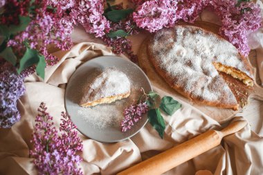 Ev yapımı elmalı turta bir kase leylağın yanındaki ahşap masada. Yumuşak tonlama. Seçici odak.
