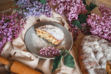 Ev yapımı elmalı turta bir kase leylağın yanındaki ahşap masada. Yumuşak tonlama. Seçici odak.