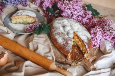 Ev yapımı elmalı turta bir kase leylağın yanındaki ahşap masada. Yumuşak tonlama. Seçici odak.