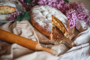Ev yapımı elmalı turta bir kase leylağın yanındaki ahşap masada. Yumuşak tonlama. Seçici odak.