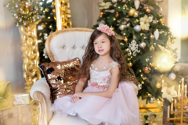 Vánoční oslava. Roztomilá holčička v krásné šaty sedí u vánočního stromu. Vánoční zázraky. Luxusní vánoční dekorace. — Stock fotografie