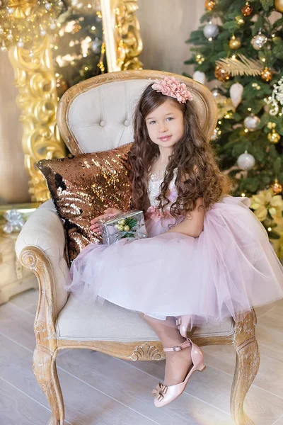 크리스마스 축 하입니다. 크리스마스 트리 근처에 앉아 아름 다운 드레스에 귀여운 작은 소녀. 크리스마스의 기적 고급 스러운 크리스마스 장식. — 스톡 사진