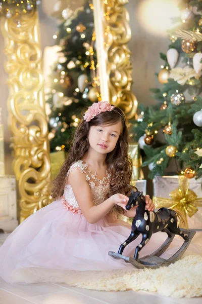 Celebração de Natal. Menina bonito em um vestido bonito sentado perto da árvore de Natal. Milagres de Natal. Luxuosa decoração de Natal . — Fotografia de Stock