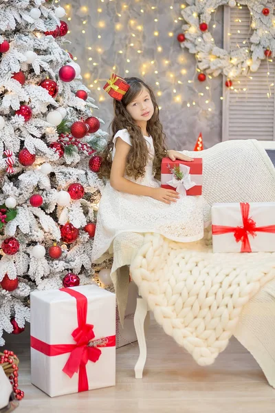 Χριστουγεννιάτικη γιορτή. Το χαριτωμένο μικρό κορίτσι σε ένα όμορφο φόρεμα που κάθονται κοντά το χριστουγεννιάτικο δέντρο. Χριστουγεννιάτικα θαύματα. Πολυτελή Χριστουγεννιάτικη διακόσμηση. — Φωτογραφία Αρχείου
