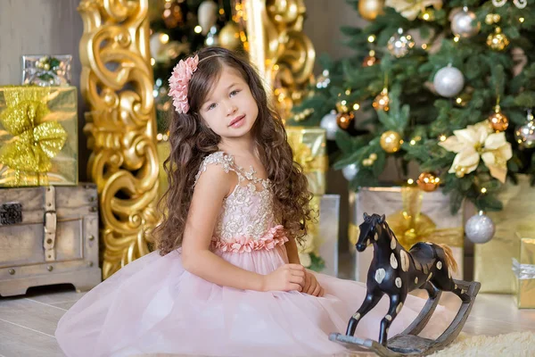Celebração de Natal. Menina bonito em um vestido bonito sentado perto da árvore de Natal. Milagres de Natal. Luxuosa decoração de Natal . — Fotografia de Stock