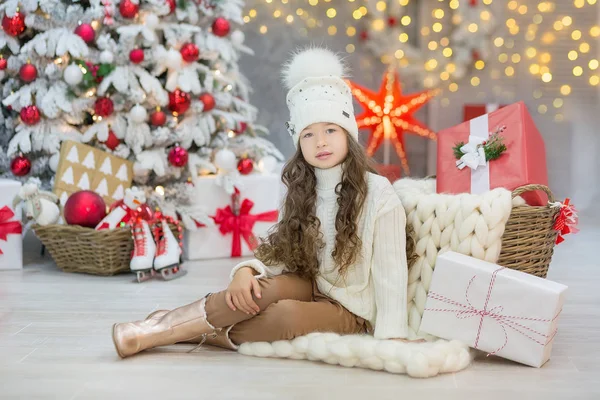 Weihnachtsfeier. niedliches kleines Mädchen in einem schönen Kleid, das in der Nähe des Weihnachtsbaums sitzt. Weihnachtswunder. Luxuriöse Weihnachtsdekoration. — Stockfoto